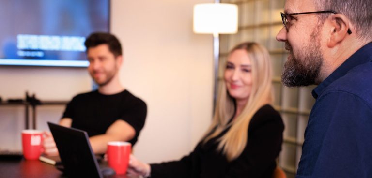 An AAB meeting with three people sitting around a table with laptops and mugs