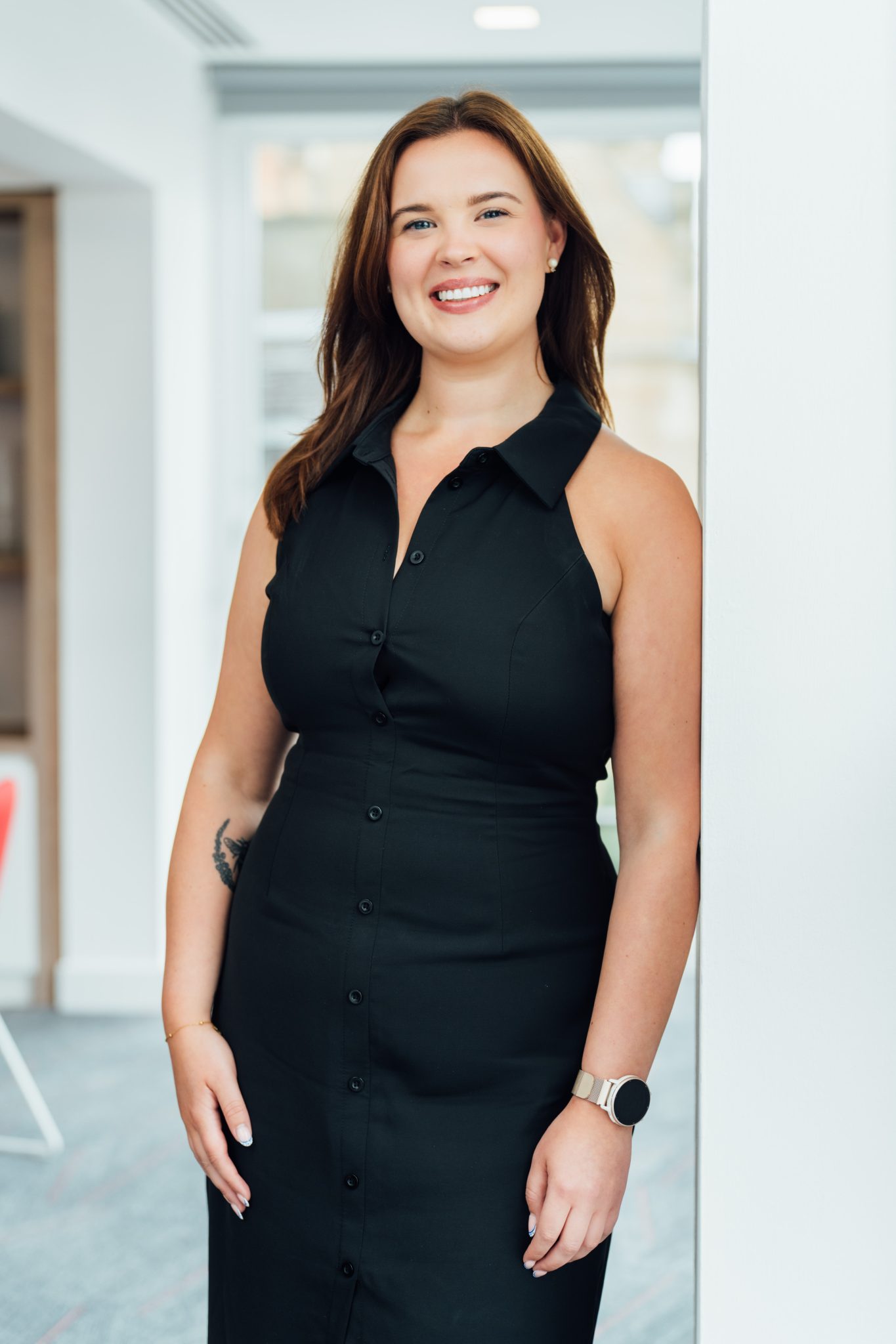 An image of Alex Brown wearing a black dress and standing against the wall.