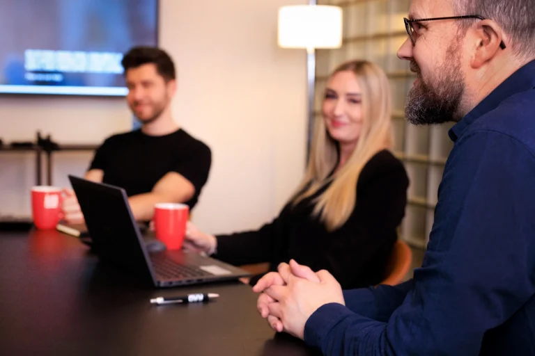 An AAB meeting with three people sitting around a table with laptops and mugs.