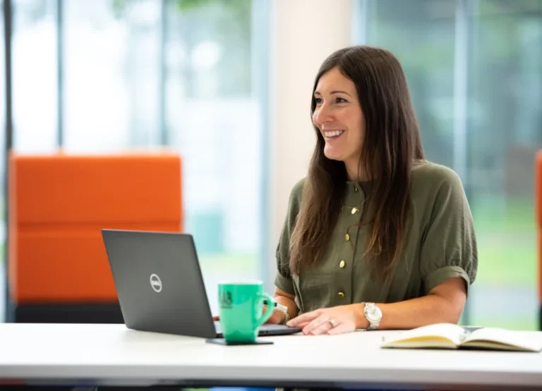 AAB team member sitting at desk on laptop smiling.