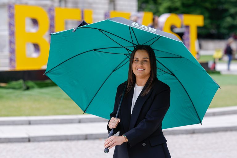 An image of an AAB employee walking outside with a black blazer and a green AAB branded umberella.