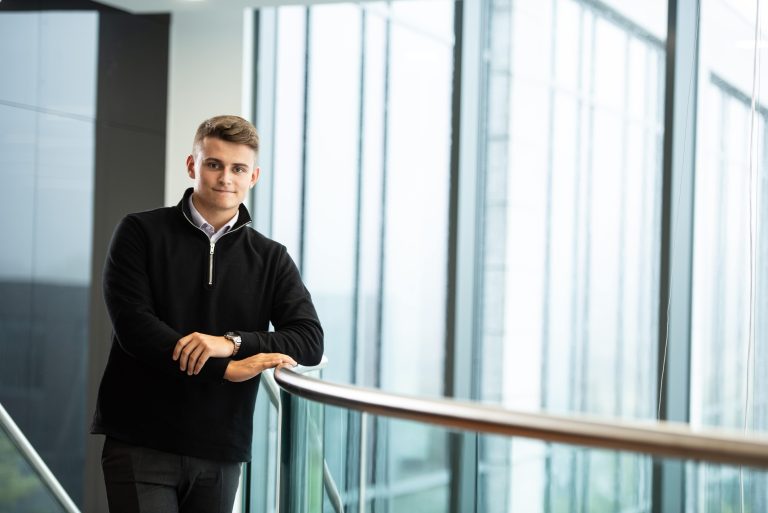 An image of an AAB employee standing on the balcony of the AAB office and wearing a dark coloured outfit. He is smiling at the camera.