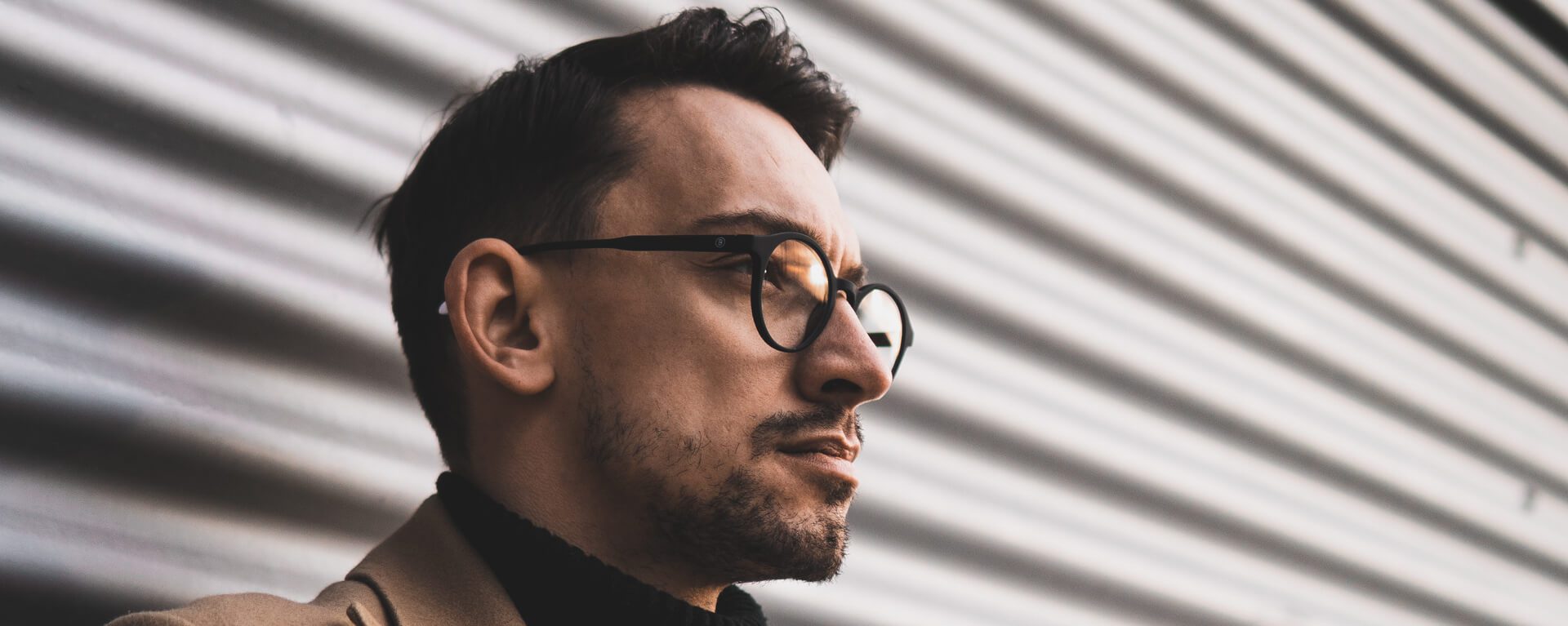 An image of a man wearing glasses with dark hair and looking out into the distance.