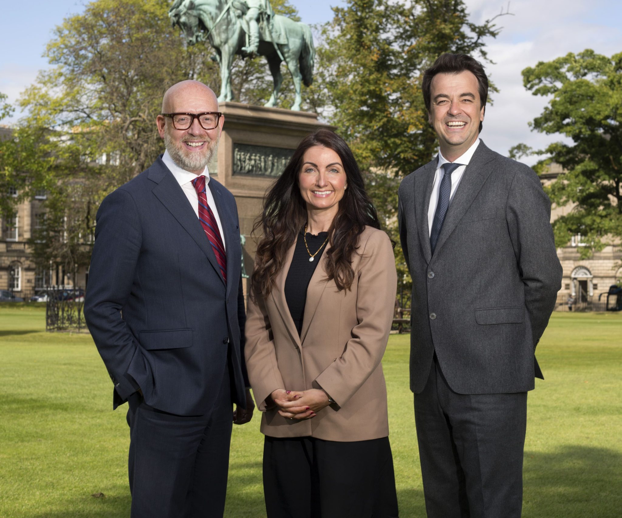 An image of Andrew, Duncan and Helen standing outside and smiling for a photoshoot amongst greenery.