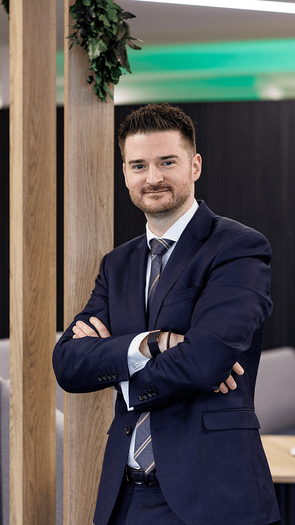 An image of Andrew Wheelan standing in the office in a suit with his arms folded.