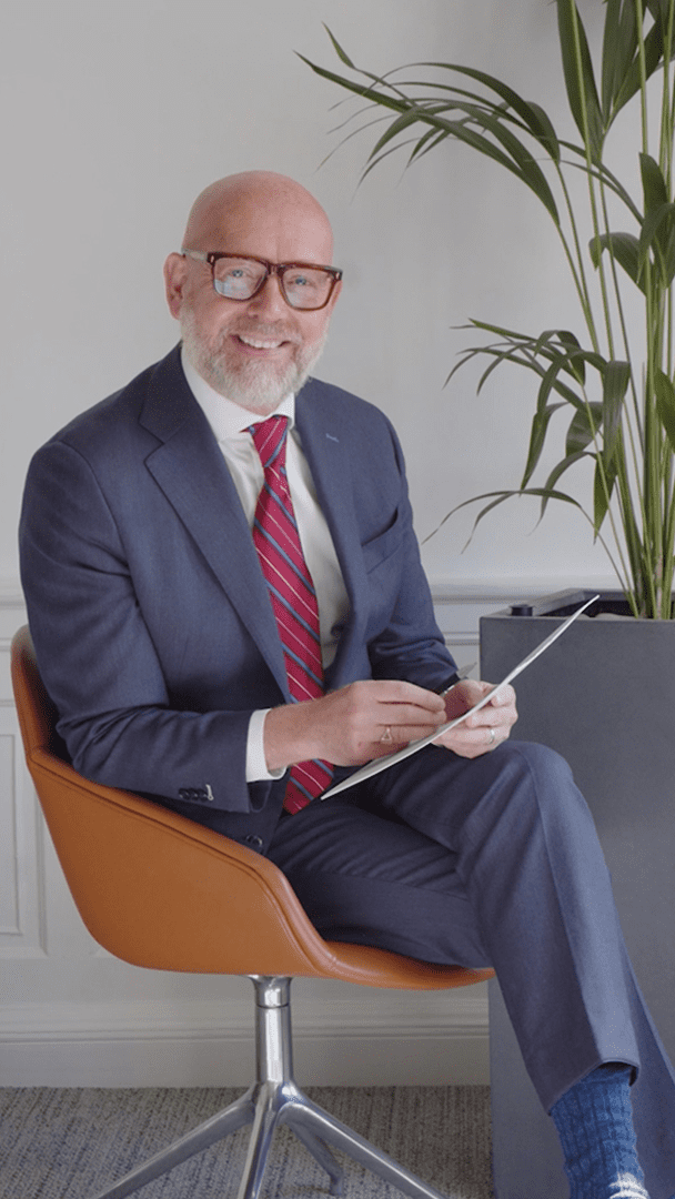 An image of Duncan sitting in the office wearing a suit and writing in a notebook.