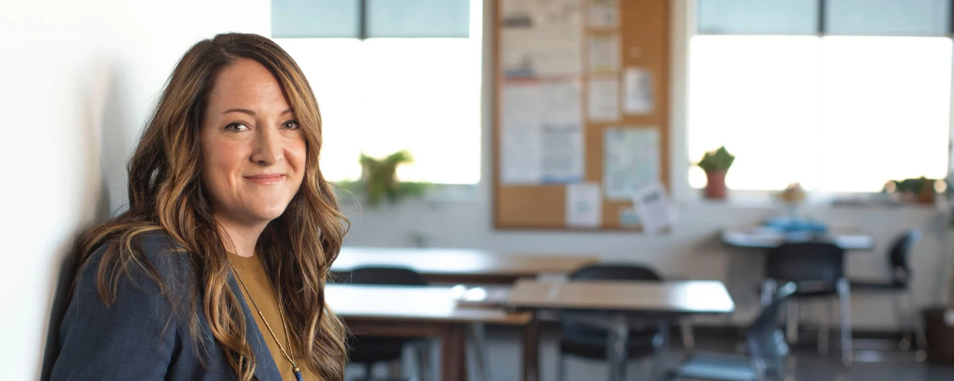 Image of a woman standing against a wall with a classroom as a backdrop.