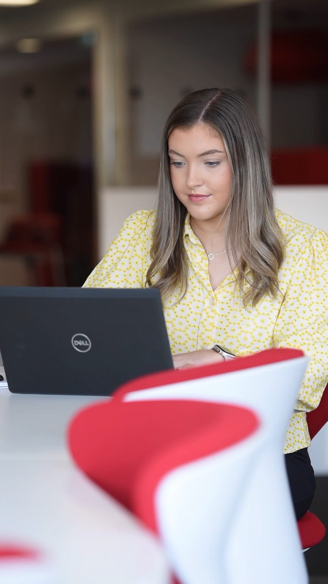 An image of Robyn Whelan sitting at a desk on her laptop and wearing a yellow top.