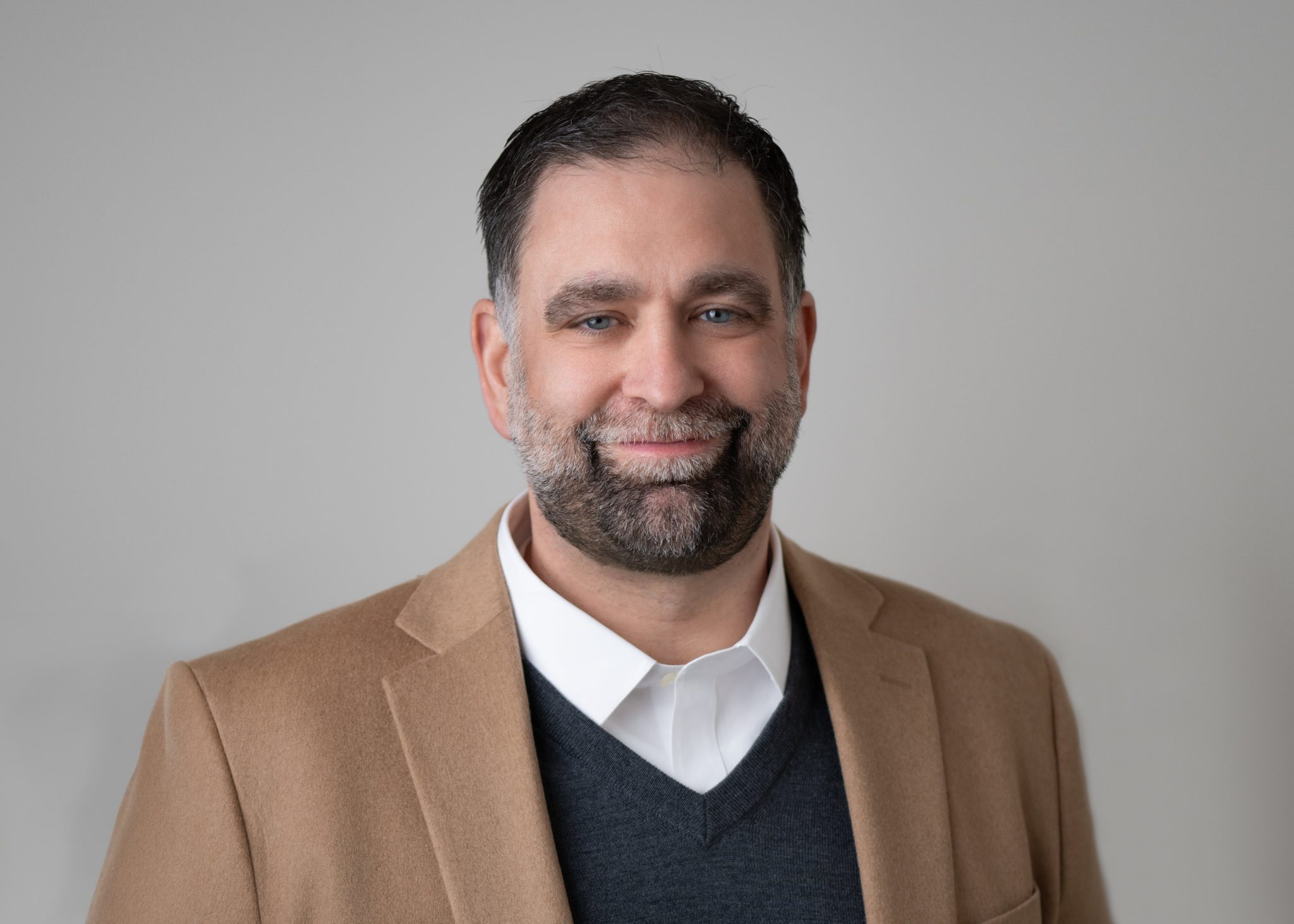 An image of Chris Andree standing against a grey background wearing a suit and shirt.