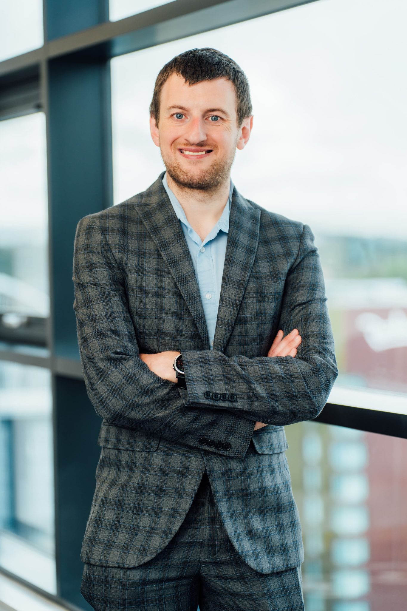 An image of Iain Litter wearing a suit with a blue shirt. His hands are crossed and he is smiling at the camera.