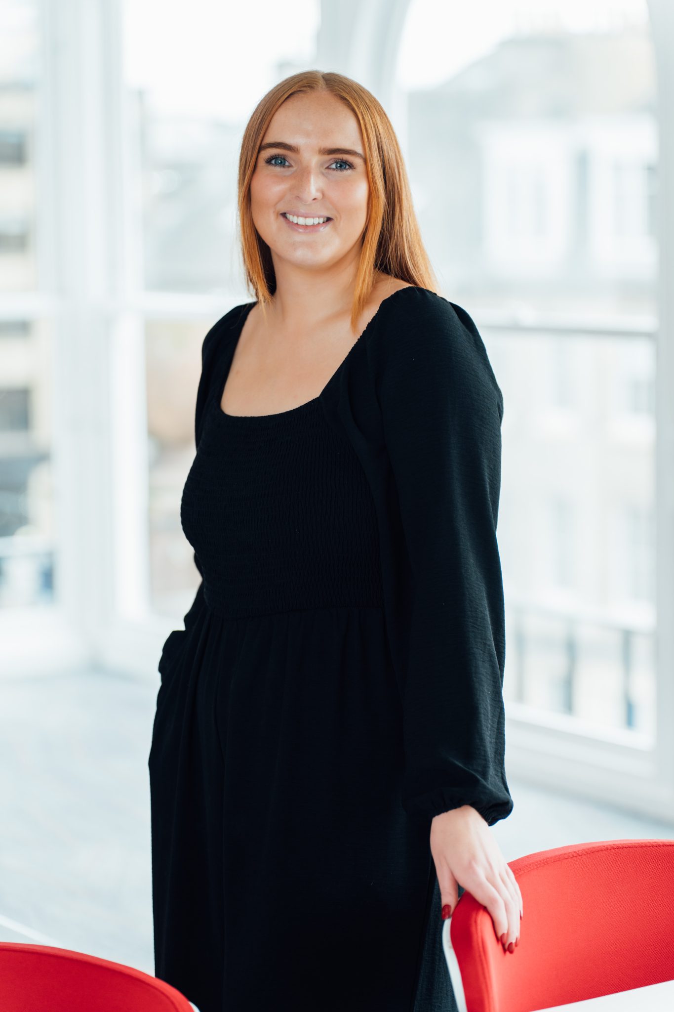 An image of Becky Weir standing in the office and wearing a black dress.
