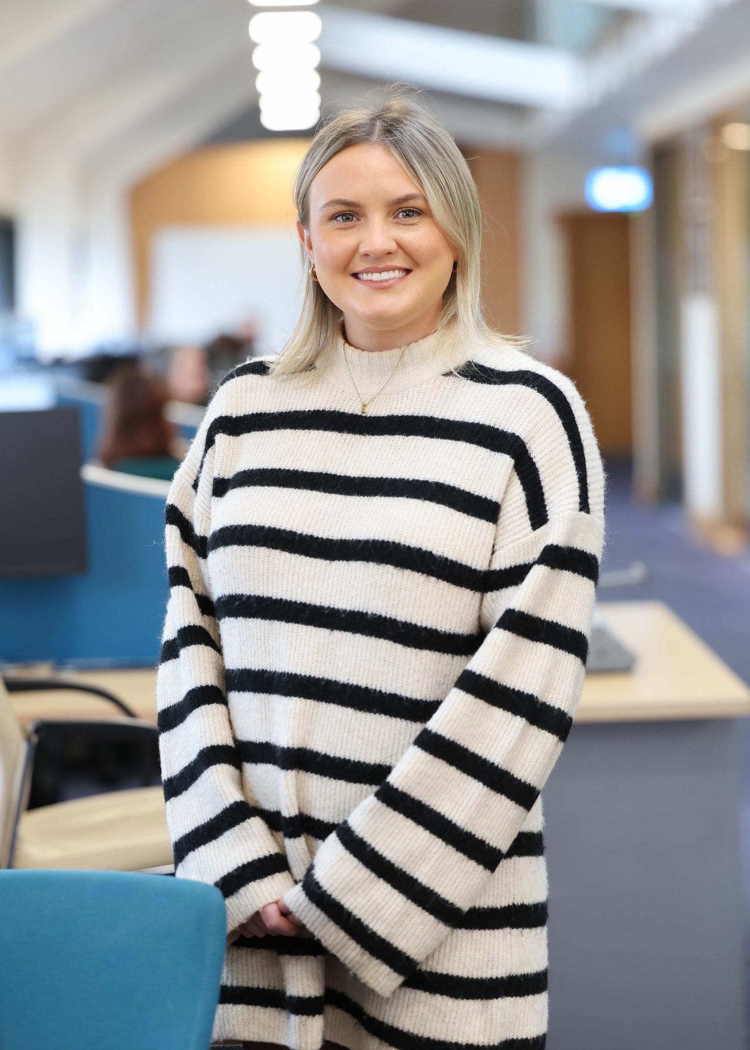 An image of Laura O'Hagan wearing a black and white stripe jumper. She is standing in the Dublin office with her hands closed.