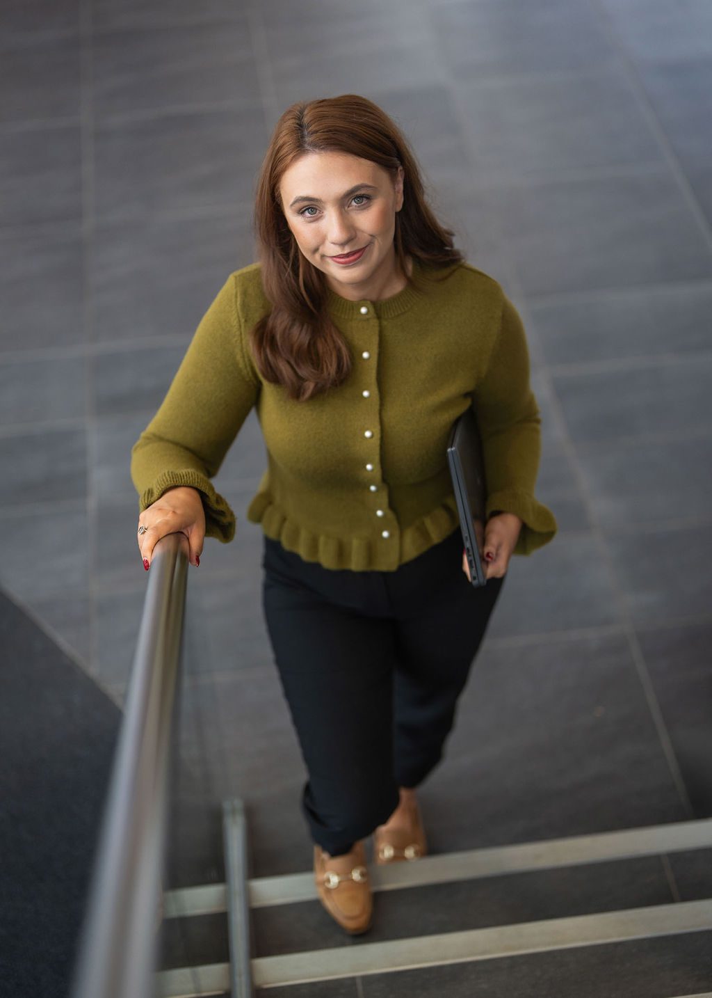 An image of Nadia Anderson wearing a green top with black trousers. Shes smiling at the camera and walking up the stairs