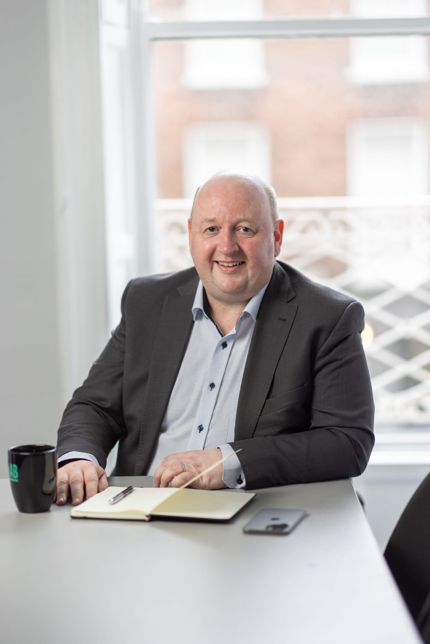 An image of Aidan McCarthy wearing a grey blazer and blue shirt. He is smiling at the camera.