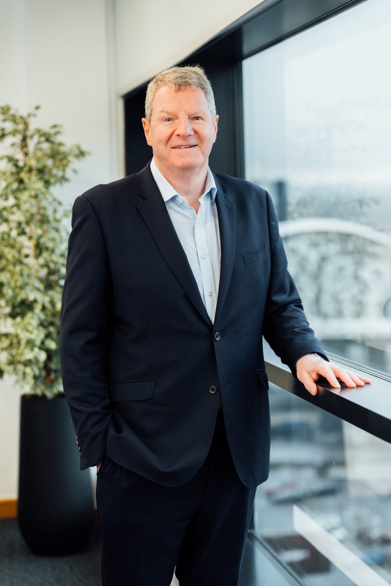 An image of Gary Harding standing in the Glasgow office wearing a suit and shirt. He is smiling at the camera.