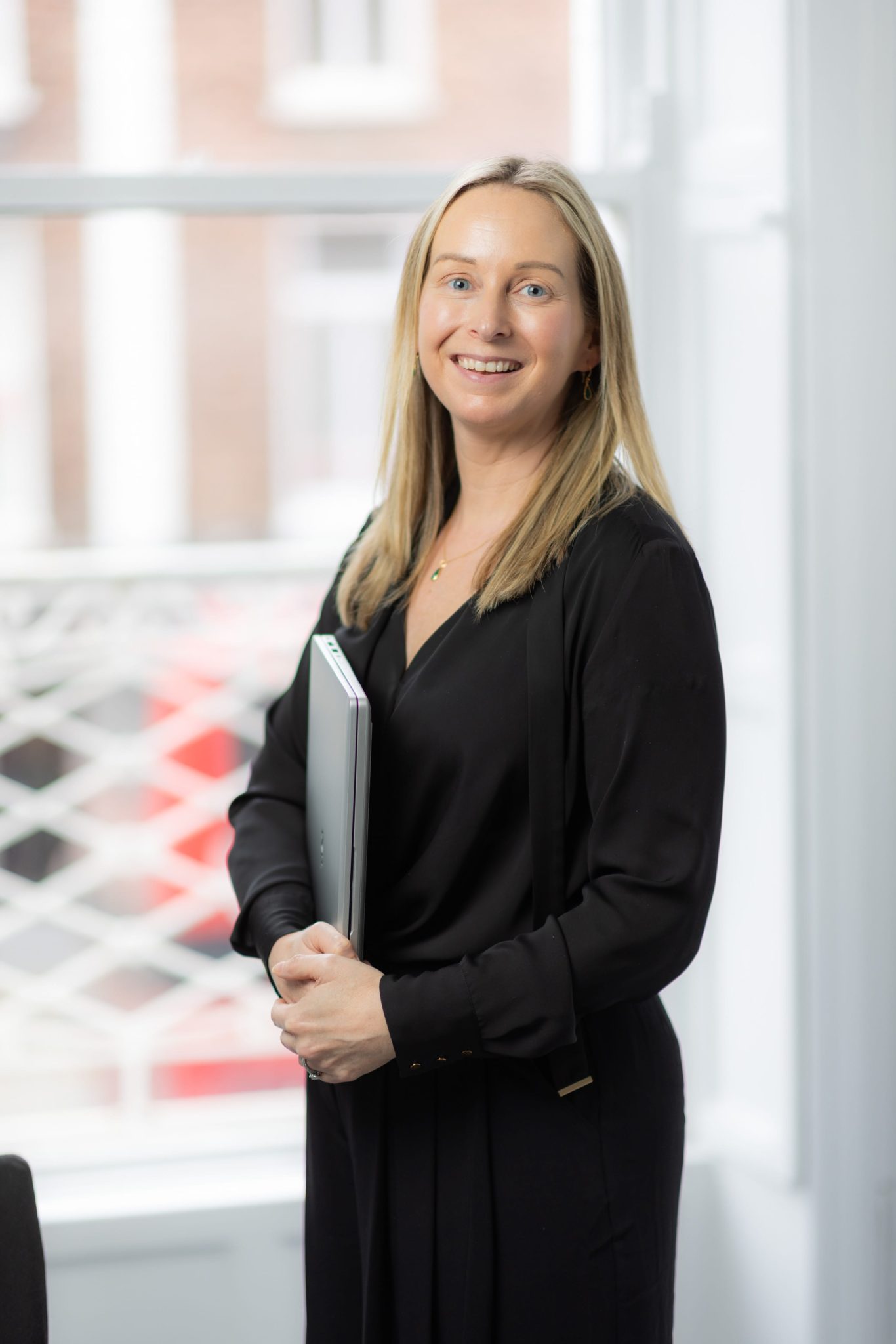 An image of Kate Mullahy wearing a black outfit and holding her laptop.