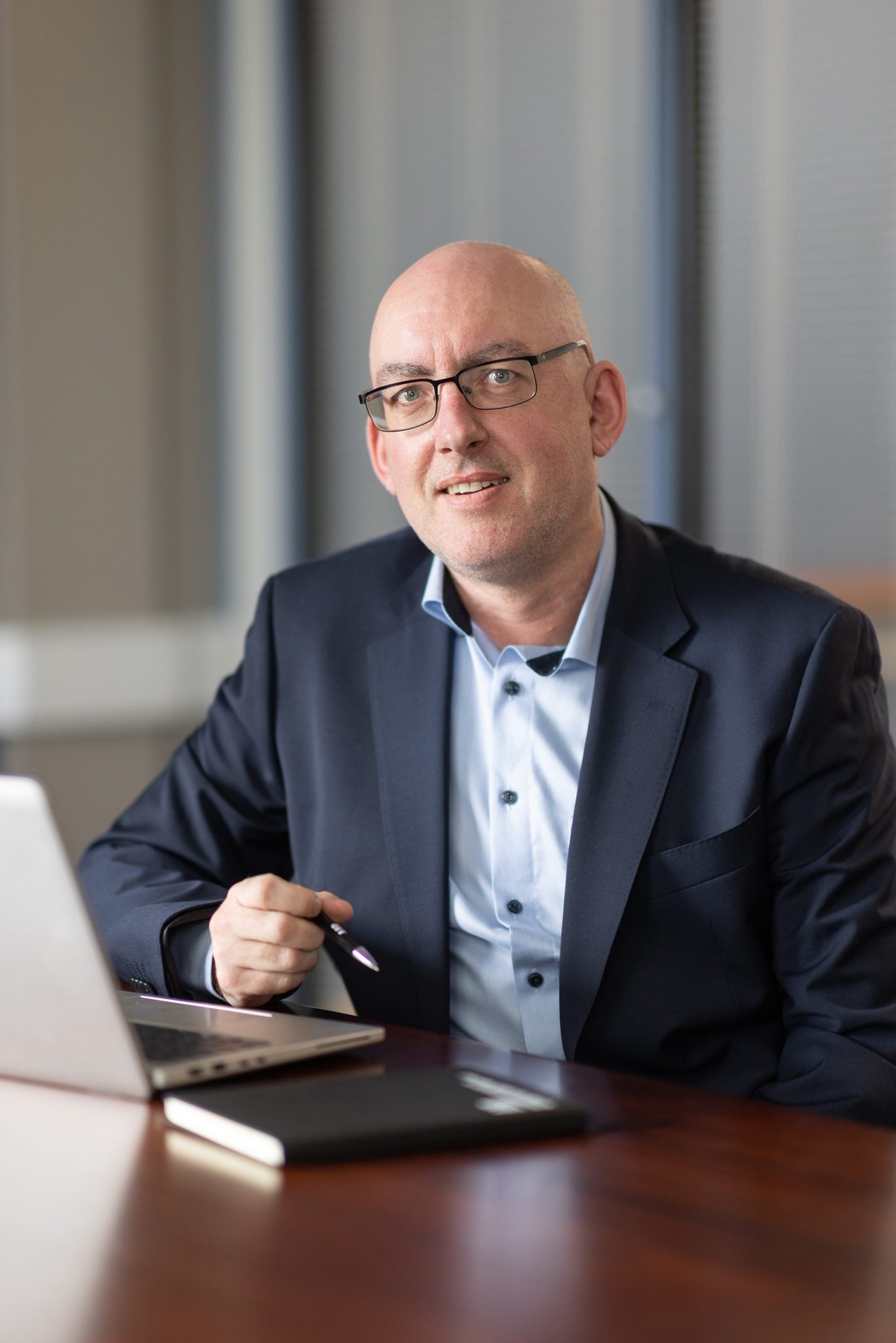 An image of Aidan McGrath wearing a blazer and shirt. Hes smiling at the camera and writing on his laptop.