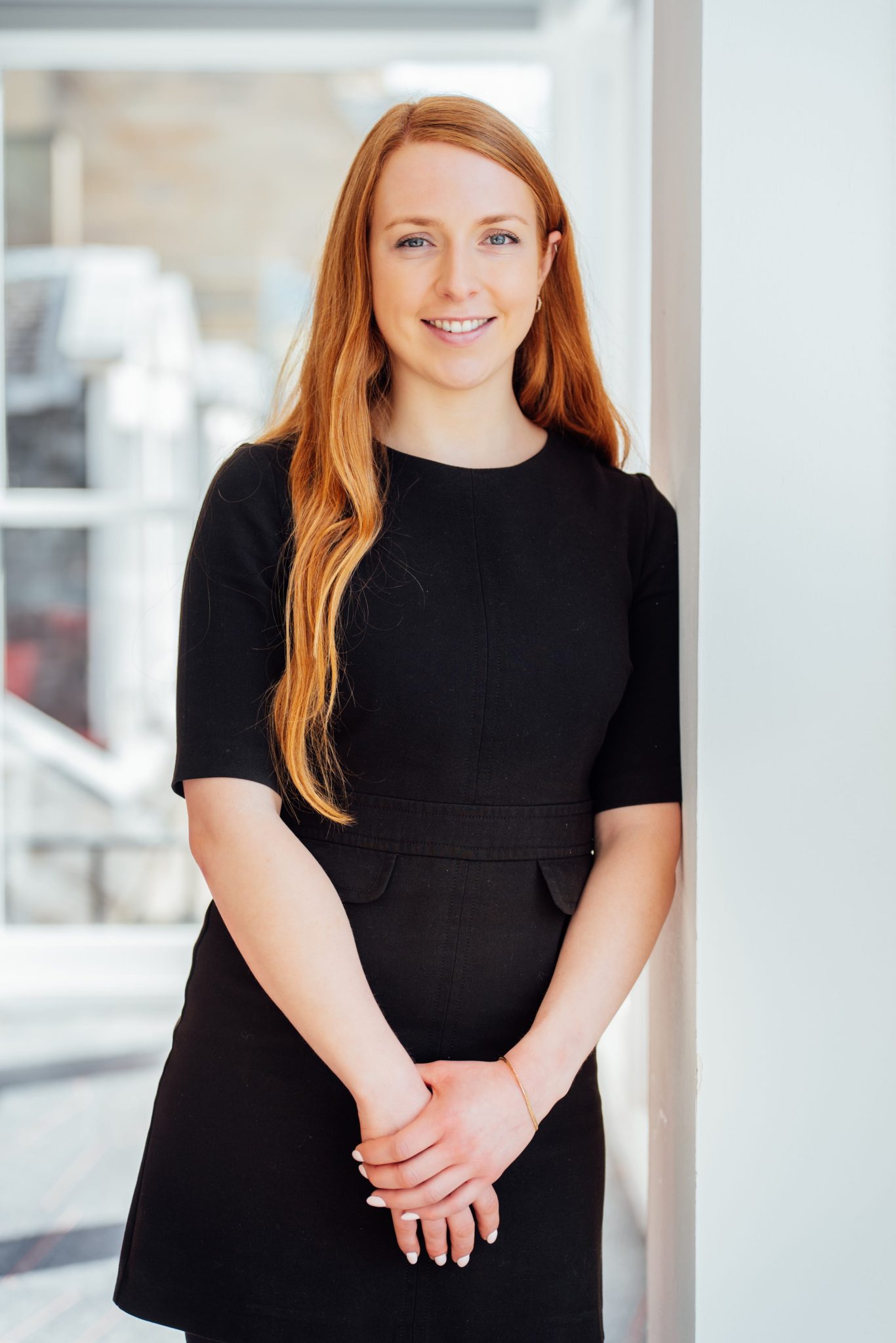 An image of Jen Armstrong standing in the office with her hands clasped and wearing a black dress.