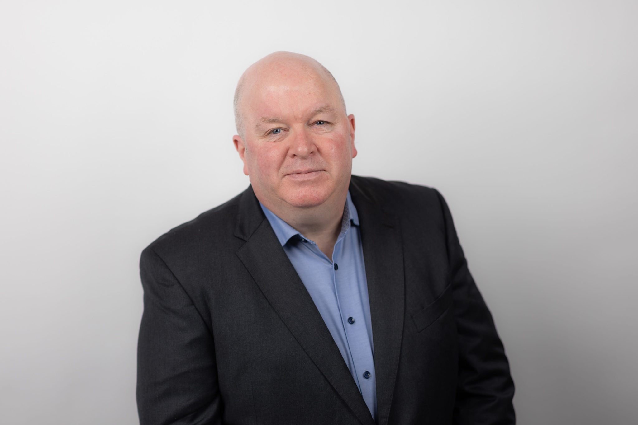 An image of Justin Brady wearing a black suit jacket with a blue shirt. He is smiling at the camera.