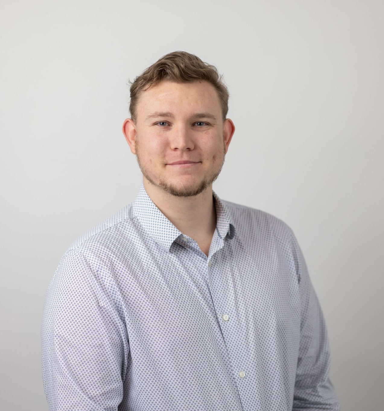 An image of Shane Brown smiling at the camera and wearing a blue shirt.