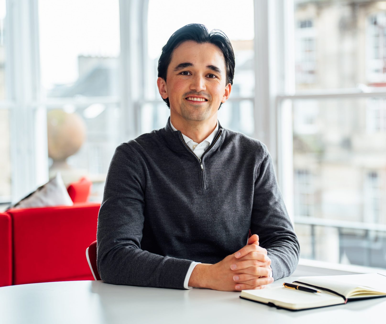 An image of Connor Sproule sitting at a desk and smiling at the camera.
