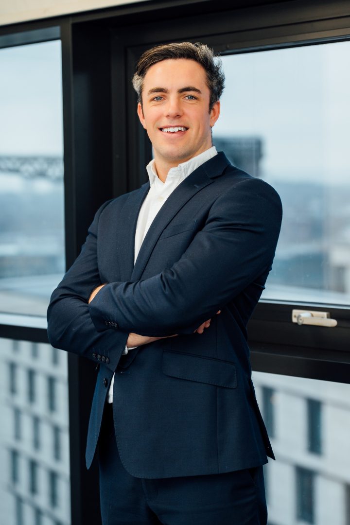 Daniel Lightbody standing with his arms folded smiling at the camera with windows behind him