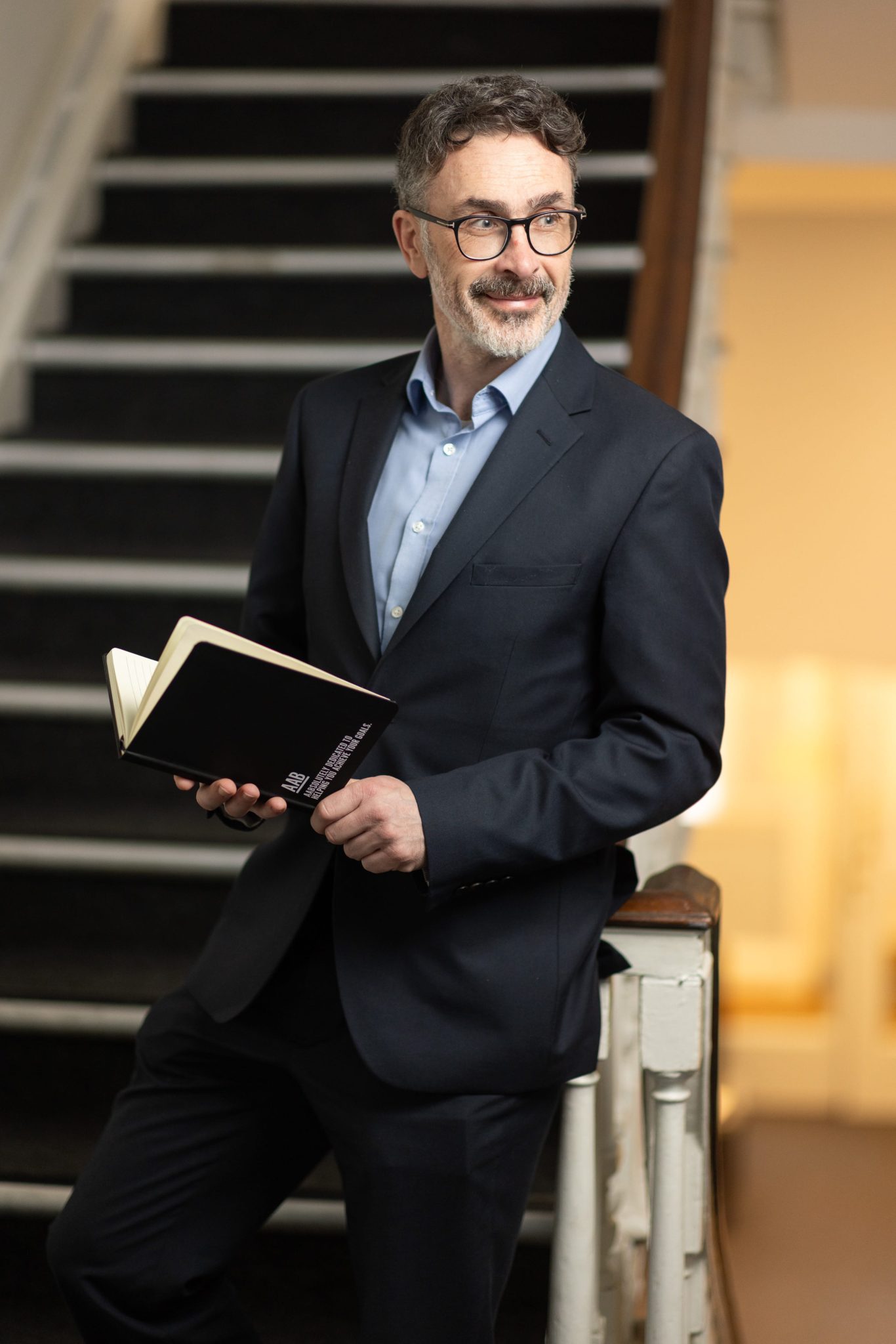 An image of Darren Benham leaning against the stairs and holding an AAB notebook.