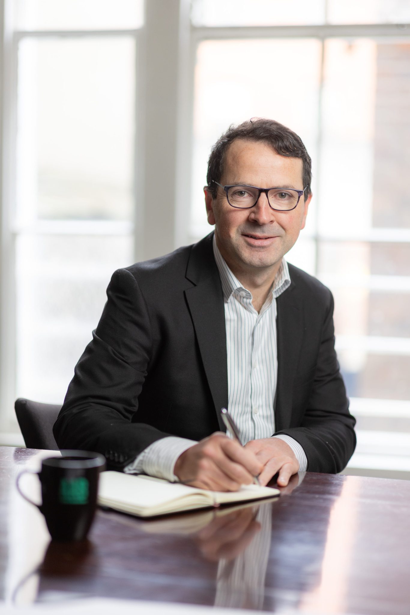An image of Eddie Conway sitting at his desk writing in his notebook and smiling at the camera.
