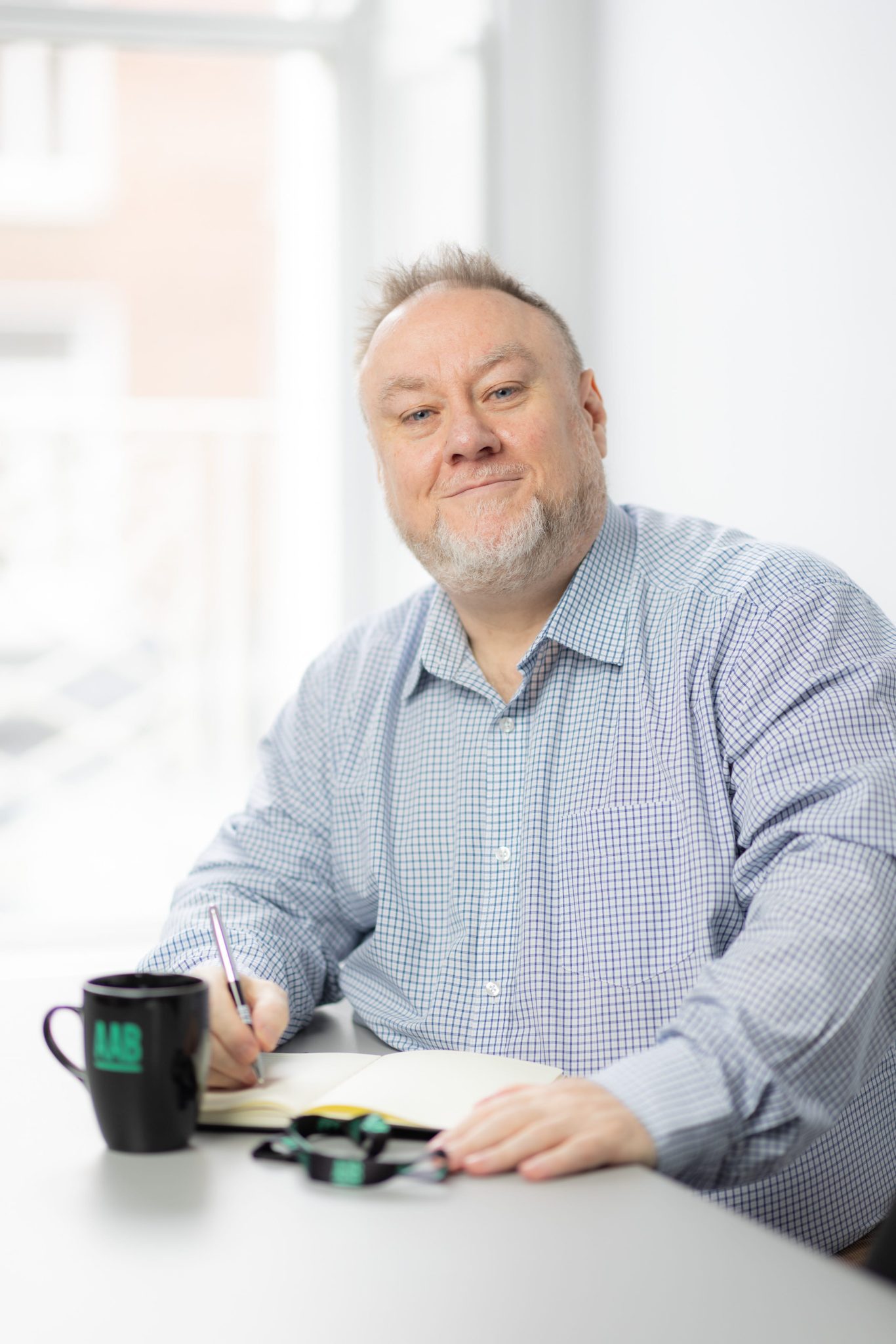 An image of Richard Maloney sitting at an office desk with their AAB mug.
