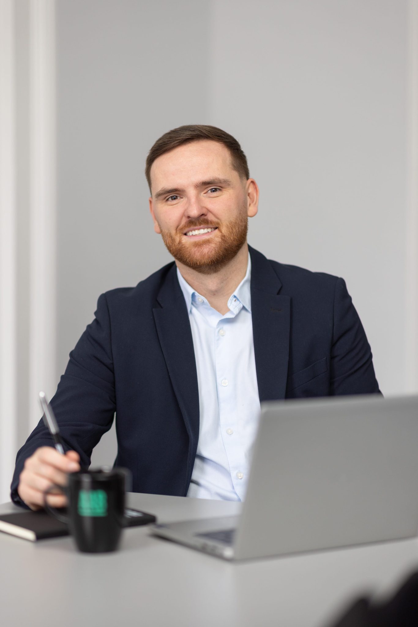 An image of Ronan Dunne sitting at a desk with their AAB mug and laptop.