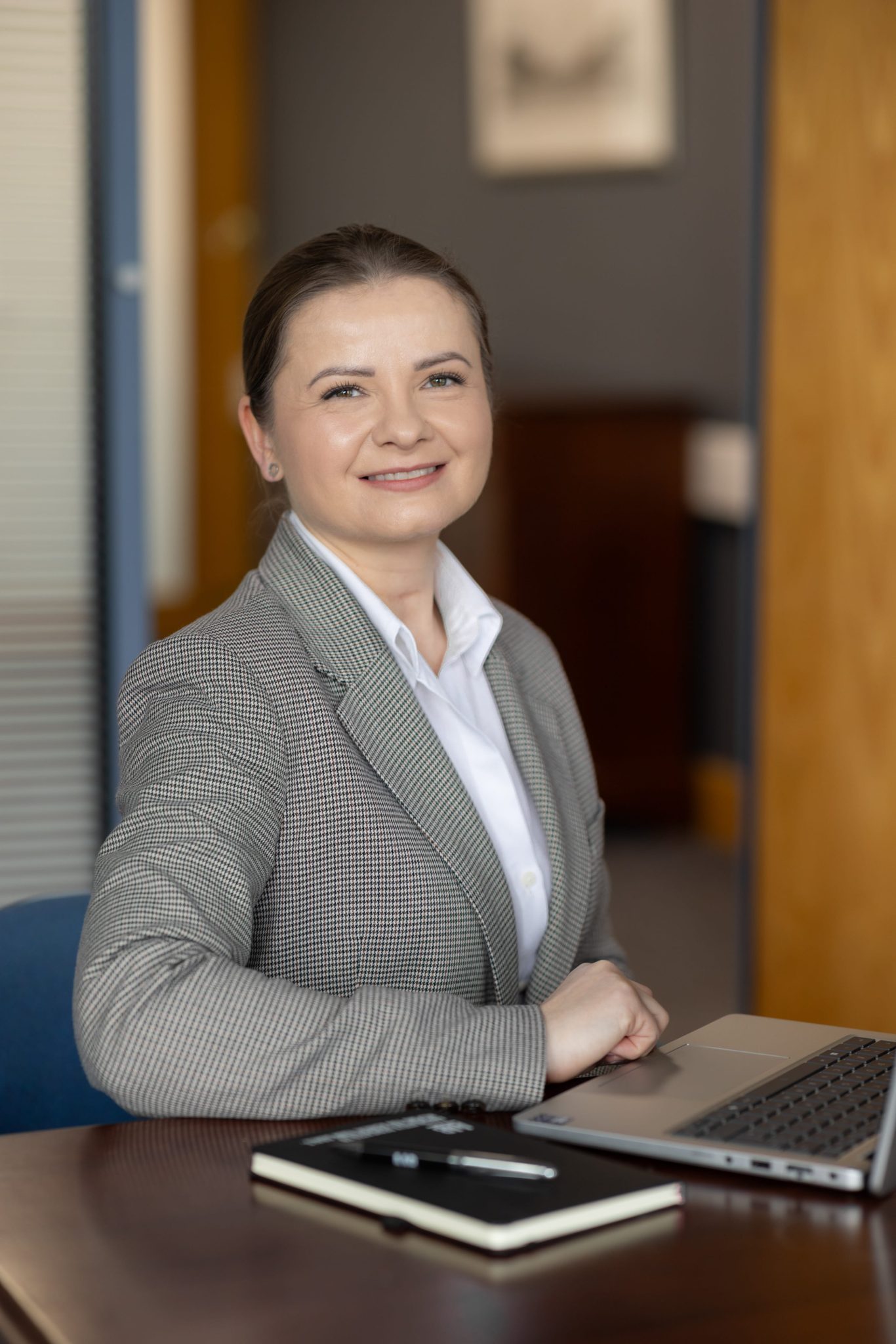 An image of Zoe Podraza Ostrega wearing a grey suit jacket and a white shirt. She is sitting at a desk with her AAB notebook,