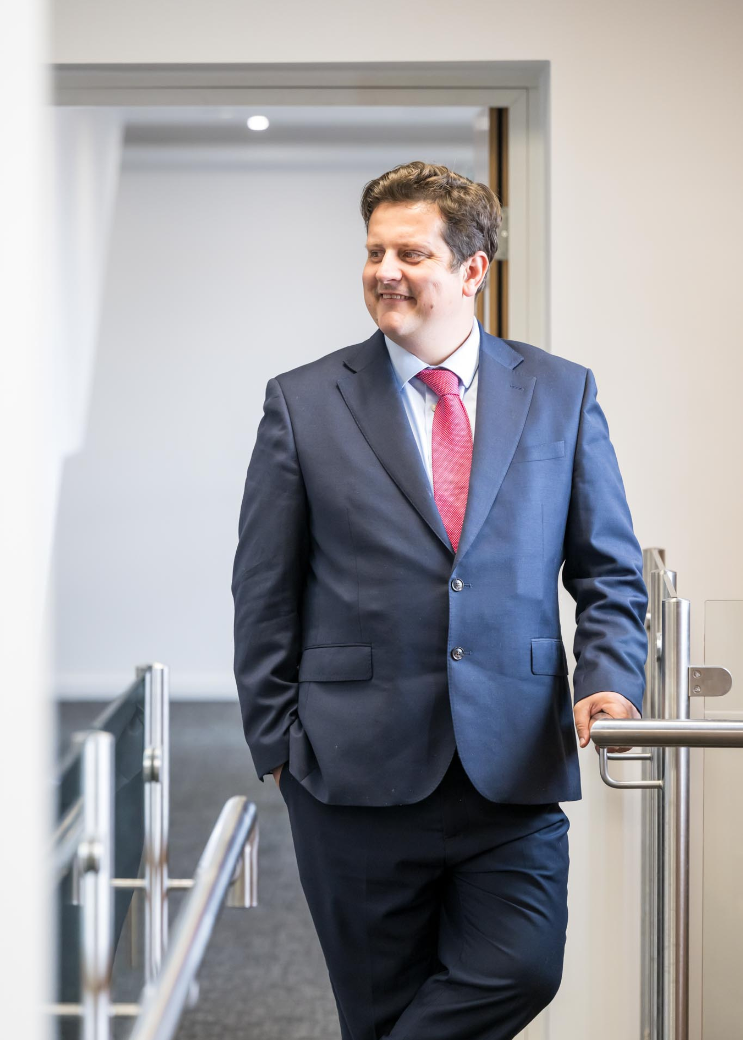 Nicholas Griffin Commercial Director leaning on a banister in a white corridor in an office