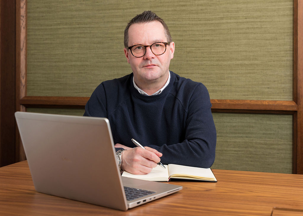 An image of Damien Crick smiling at the camera with his laptop.